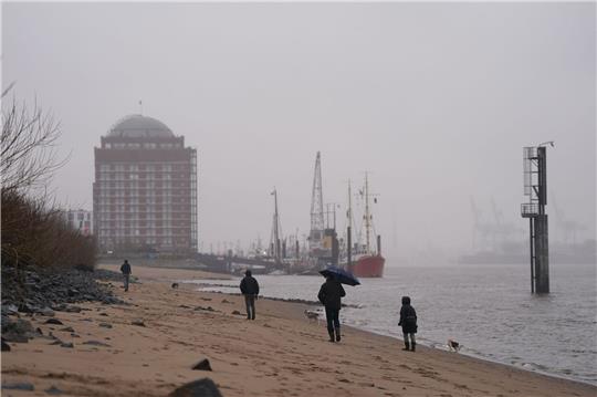 Passanten gehen im strömenden Regen am Elbstrand in Ovelgönne spazieren.