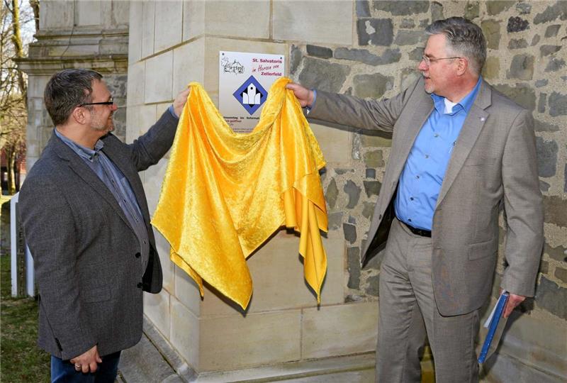 Pastor André Dittmann (li.) und Diakon Jürgen Lojowsky von der Landeskirche Hannovers enthüllen das Signet am Kircheneingang.  Foto: Müller