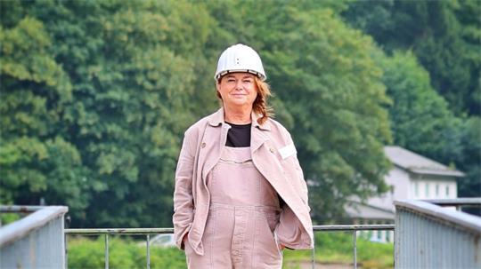 Eine Frau in Grubenführer-Kluft und Schutzhelm lächelt in die Kamera.