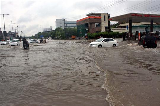 Pendler fahren in Lahore eine überschwemmte Straße entlang.