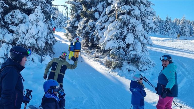 Familien stehen vor einer verschneiten Landschaft mit ihrem Ski-Equipment.