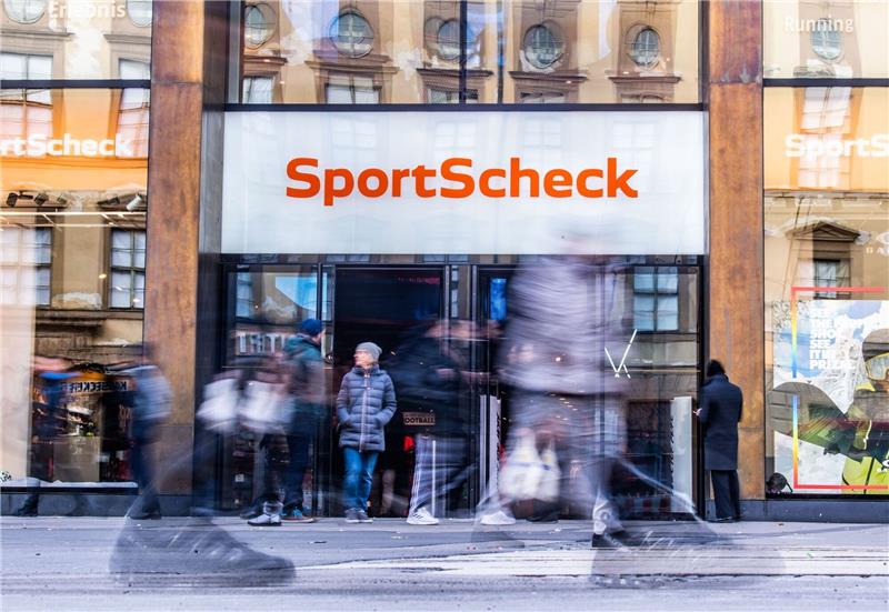SportScheck-Geschäfte schließen: 200 Arbeitsplätze weniger Personen gehen an einer Sportscheck-Filiale in der Münchener Fußgängerzone vorbei.