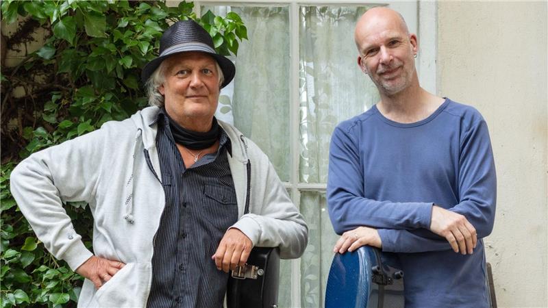 Zwei Männer mit Gitarrenkoffern gucken in die Kamera.