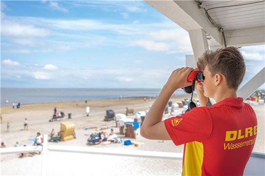 Peter von der DLRG-Wasserrettung steht auf einem Turm und beaufsichtigt mit einem Fernglas den Badestrand von Dangast.