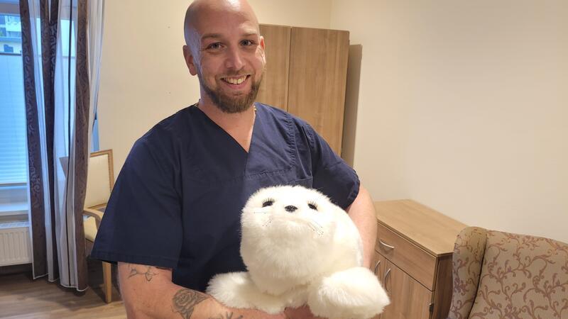 Pflegefachkraft Kevin Kühl zeigt die Paro-Robbe. Sie kommt hauptsächlich an den Betten der Patienten zum Einsatz.