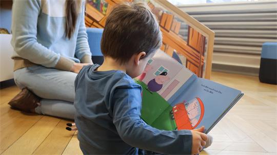 Auf dem Bild ist ein Kind von hinten zu sehen, das in einem Kinderbuch blättert.