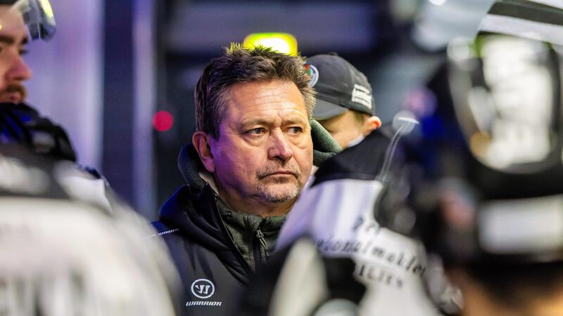 Mehrere Personen in Eishockeykleidung und Helmen, eine Person trägt eine Jacke mit dem Logo "Warrior"