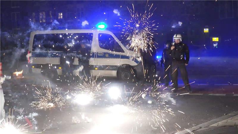 Polizeibeamte stehen in der Silvesternacht 2022 in Berlin hinter explodierendem Feuerwerk.