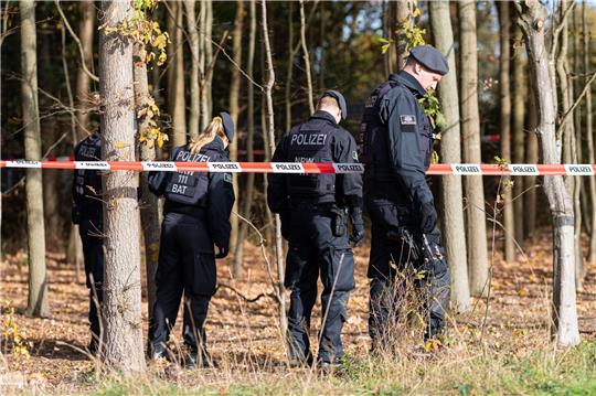 Polizisten hinter einem Polizeiabsperrband durchsuchen das Gelände, in dem am Morgen eine 13jährige bewusstlos aufgefunden worden war.