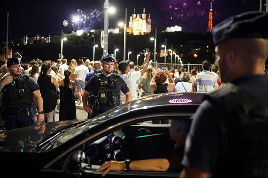 Polizisten kontrollieren einen Autofahrer in Lyon, während die Menschen ein Feuerwerk zum Tag der Bastille beobachten.