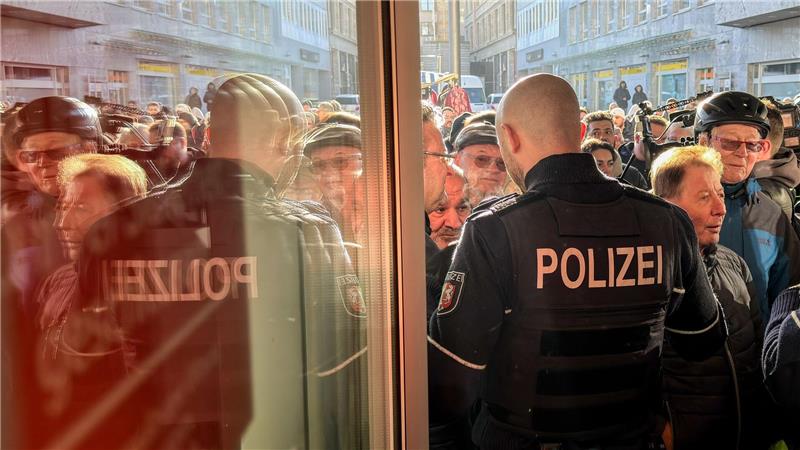 Polizisten sichern den Eingang der Sparkassenfiliale in Gelsenkirchen, vor der viele besorgte Kunde stehen und Informationen nach dem Einbruch in den Tresorraum verlangen.