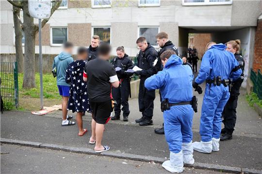 Polizisten, zum Teil in Schutzkleidung, kontrollieren Anwohner vor einem Wohnkomplex.