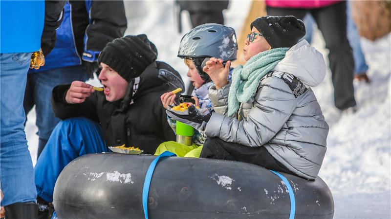 Drei Kinder sitzen auf einem aufgeblasenen Reifenschlauch und essen Pommes.