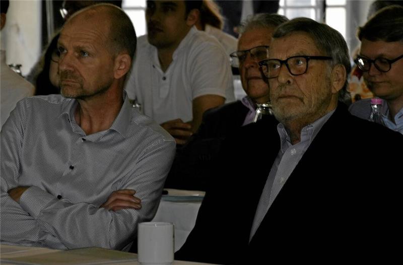 Goslarer Millionen-Deal: Schwenke de Wall verkauft an Bettels Zwei Männer sitzen nebeneinander, einer trägt ein helles Hemd, der andere einen dunklen Anzug, im Hintergrund weitere Personen.