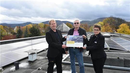 Präsentieren auf dem Dach des Plaza Inn die Tafel, die die Partnerschaft in Sachen Ökostrom dokumentiert (v.li.): Christian Mühlhausen, Klaus-Dieter Voß und Heike Kurts. Auch bei wolkenverhangenem Himmel wird hier noch Energie produziert.