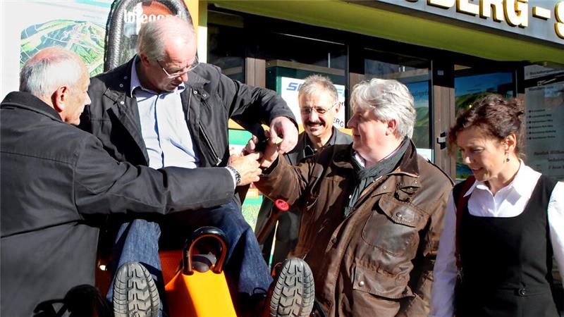 Vier Personen stehen vor der Seilbahn-Station, eine Person sitzt auf einem Rodel und lässt beim Abschnallen helfen
