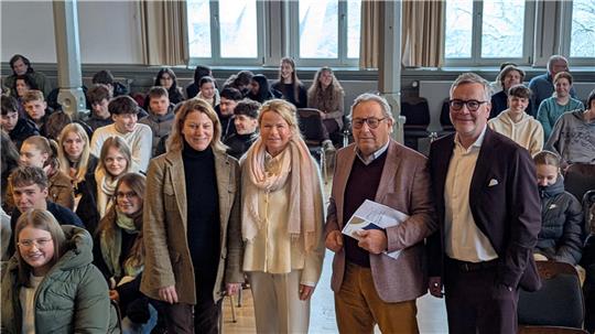 Gruppe von vier Personen steht vorne in einem Raum mit vielen sitzenden Zuschauern im Hintergrund