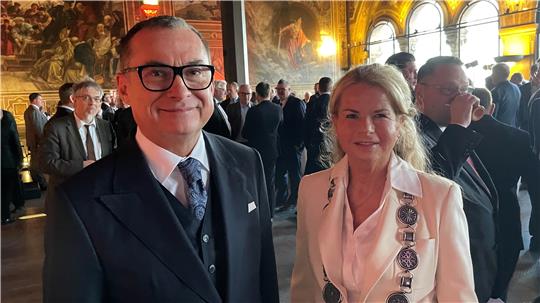 Mann im Anzug und Krawatte vor einem Gebäude mit einem blauen Schild der Deutschen Bundesbank und gelben Sternen