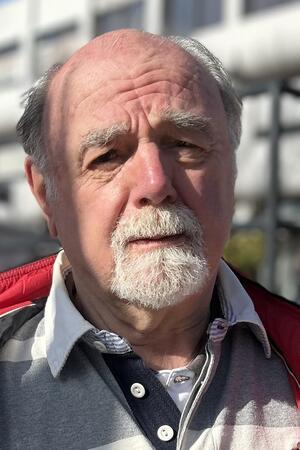 Postbank-Schließung: Das sagen Kunden, die FDP will eine Petition Älterer Mann mit grauem Hemd unter einem dunkelblauen Pullover und roter Jacke im Freien vor einem Gebäude