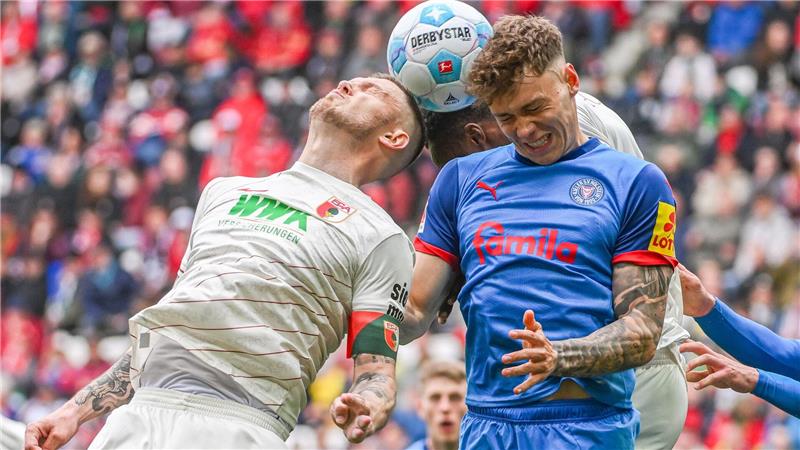 Rasant ging es zu auf dem Platz. Kiels Nicolai Remberg (r) und Augsburgs Kapitän Jeffrey Gouweleeuw beim Kopfballduell.