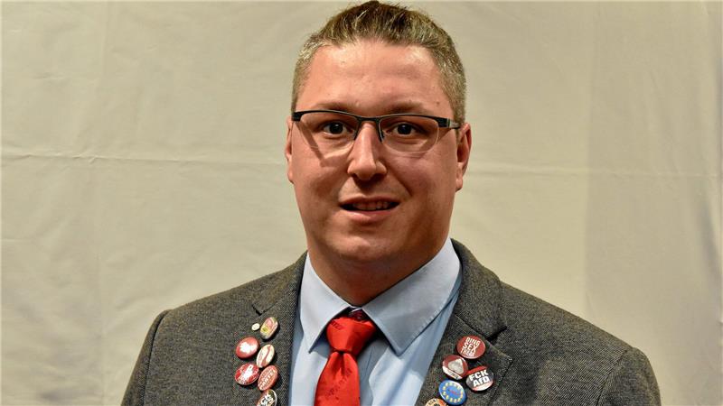 Zu sehen ist ein Mann im Anzug, in dem viele Abzeichen stecken.