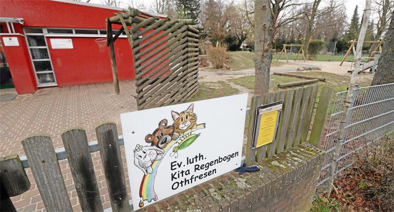 Ein rotes Gebäude mit Spielplatz daneben, im Vordergrund das Schild mit der Aufschrift "Ev. luth. Kita Regenbogen Othfresen".