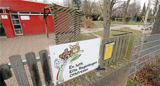 Ein rotes Gebäude mit Spielplatz daneben, im Vordergrund das Schild mit der Aufschrift "Ev. luth. Kita Regenbogen Othfresen".
