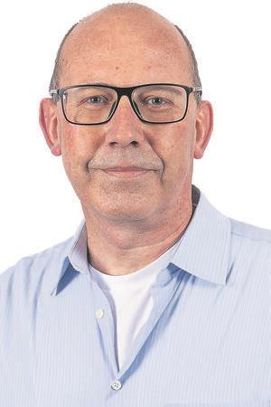 Ein Mann mit helblauem Hemd vor einer weißen Wand.