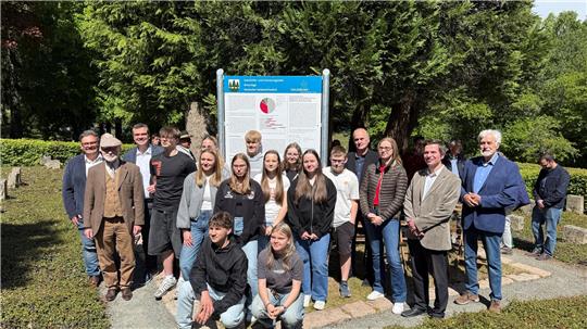 Redner (Wolfgang Langer, links, mit Dr. Rainer Bendick und Dr. Alexander Saipa daneben), Gäste und Schüler stellen sich nach dem offiziellen Teil der Einweihung für ein Gruppenfoto vor die Tafel auf dem Soldatenfriedhof.