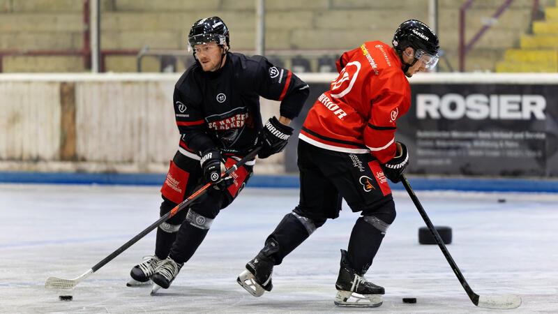 Zwei Eishockeyspieler in schwarzer und roter Ausrüstung kämpfen um den Puck auf dem Eis
