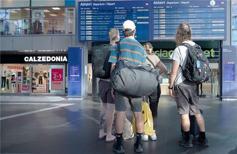 Reisende im Berliner Hauptbahnhof vor einer Info-Tafel mit Zugverbindungen.
