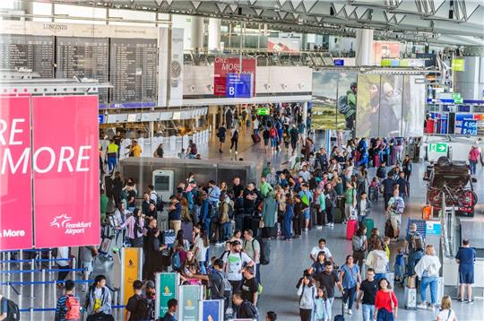 Reisende stehen am Flughafen Frankfurt Main  beim Einchecken in einer langen Schlange.