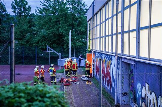 Rettungskräfte stehen vor einer Turnhalle. Vier Kinder sind durch das Dach einer Sporthalle gefallen.