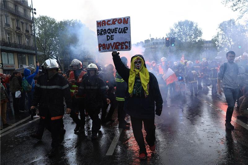 Frankreich: Ausschreitungen bei Protesten gegen Rentenreform Rettungskräfte und ein Demonstrant mit einem Plakat mit der Aufschrift «Macron, Räuber der Armen» marschieren während einer Demonstration anlässlich des Tages der Arbeit in Paris.