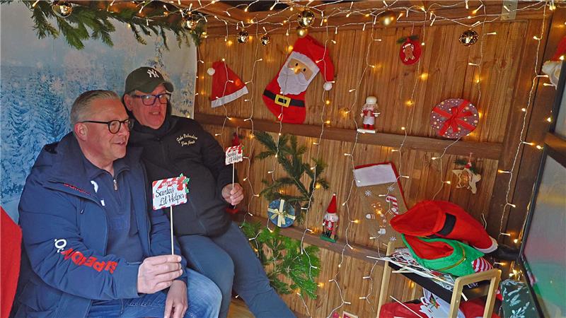 Das sagen die Schausteller zum Goslarer Weihnachtsmarkt Zwei Männer sitzen in einer weihnachtlich dekorierten Holzhütte mit Lichterketten, Weihnachtsmützen und kleinen Dekorationen an den Wänden.