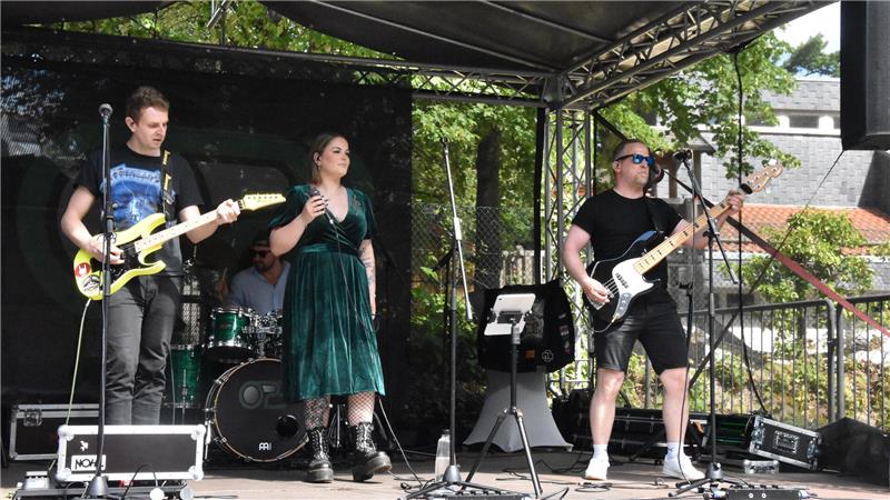Band mit Sängerin und Gitarristen spielt auf einer überdachten Bühne im Freien.