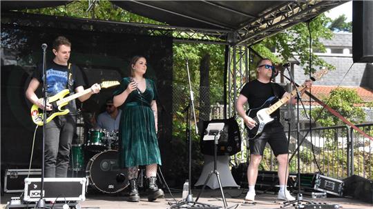 Band mit Sängerin und Gitarristen spielt auf einer überdachten Bühne im Freien.