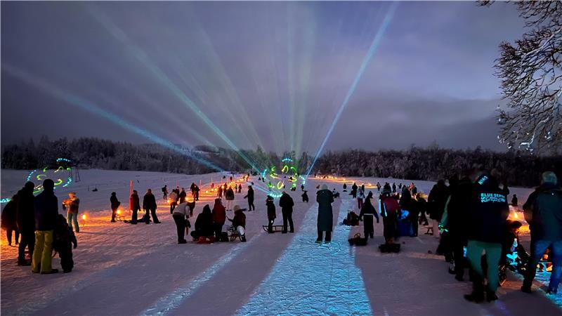 Viele Menschen beobachten eine Lichter-Show am verschneiten Rodelhang.