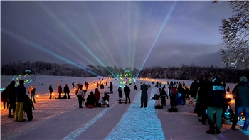 Viele Menschen beobachten eine Lichter-Show am verschneiten Rodelhang.