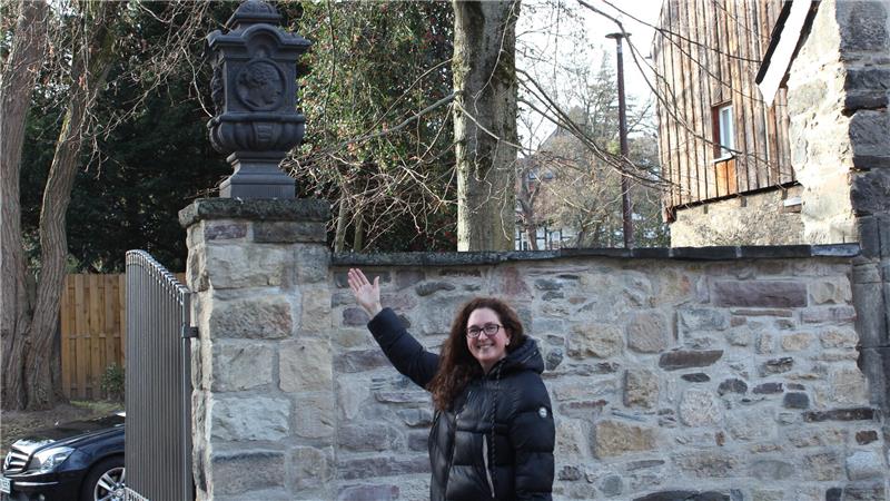 Historische Steinvase kehrt nach Jahren an Ursprungsort zurück Person in schwarzer Winterjacke steht vor einer Steinmauer mit einem dekorativen schwarzen Skulptur darauf.