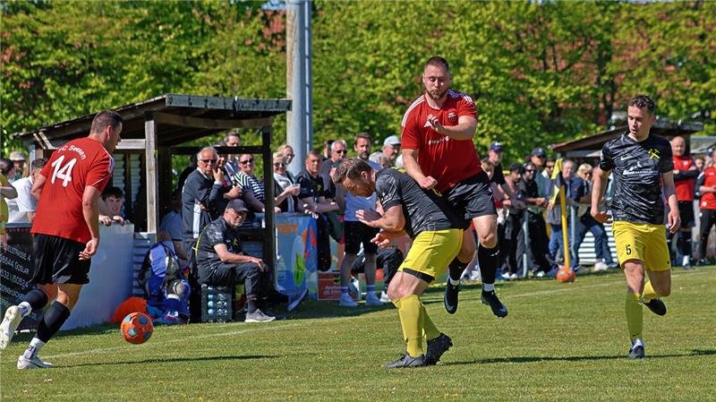 Fußballspieler in roten und schwarzen Trikots kämpfen um den Ball auf einem Spielfeld vor einer Zuschauertribüne mit vielen Zuschauern.