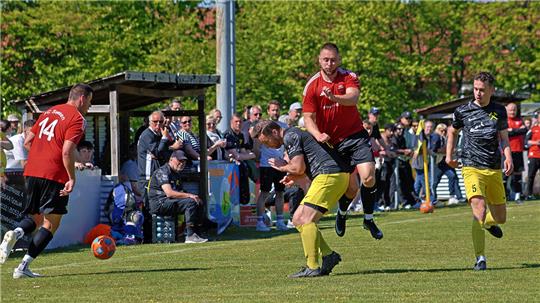 Fußballspieler in roten und schwarzen Trikots kämpfen um den Ball auf einem Spielfeld vor einer Zuschauertribüne mit vielen Zuschauern.