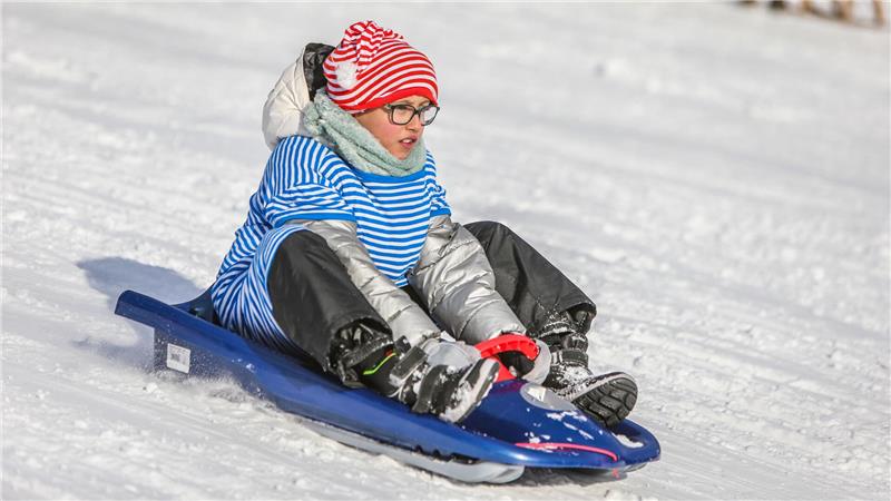 Ein Junge rodelt mit Schlafmütze und Schlafanzug verkleidet den Berg hinab.