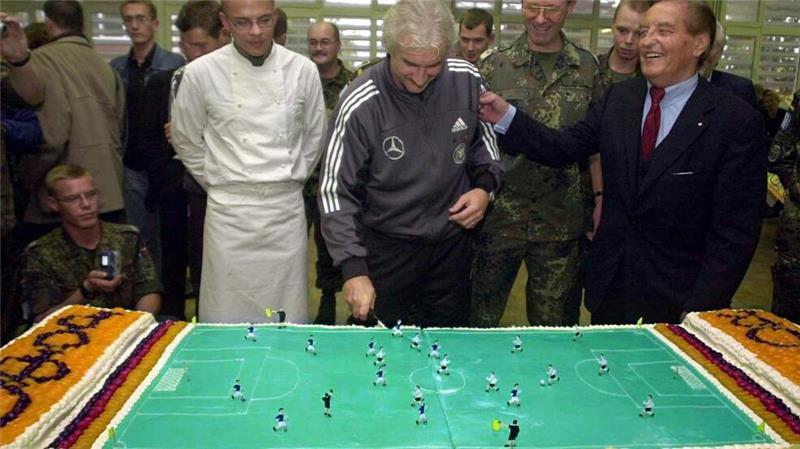 Rudi Völler (M) schneidet beim Truppenbesuch in Sarajevo eine Torte in Form eines Fußallplatzes an.