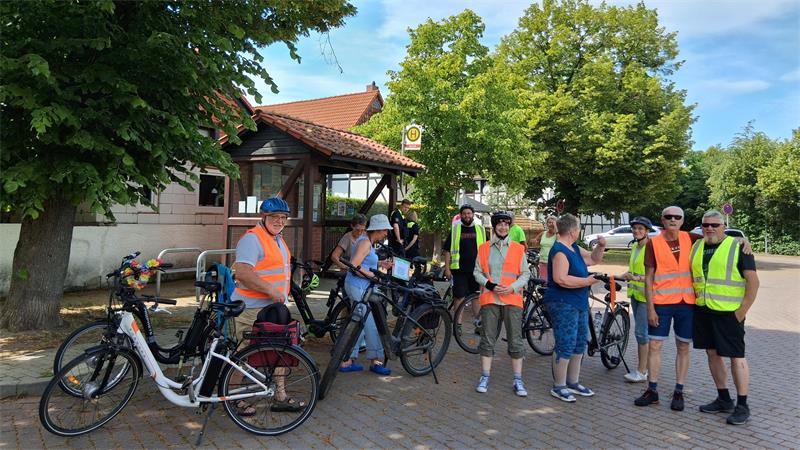 Gruppe von Menschen mit Fahrrädern und Warnwesten steht auf gepflastertem Platz vor Fachwerkhaus und Bäumen