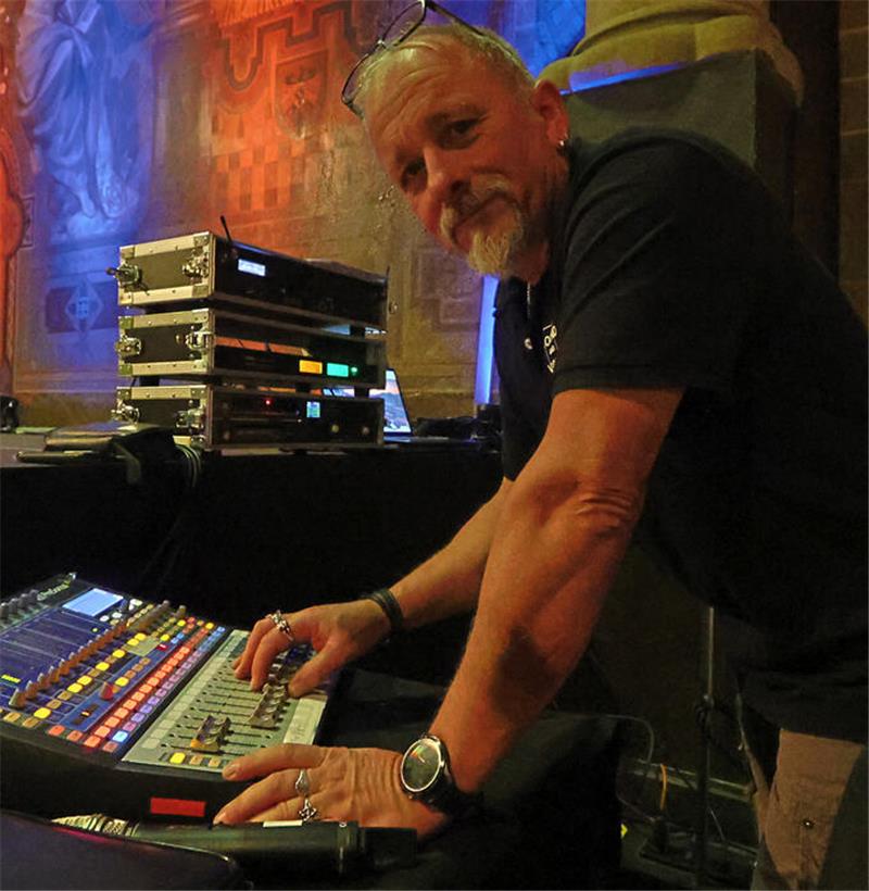 Mann bedient ein Mischpult in einem festlich beleuchteten Raum mit Wandmalereien und Säulen.