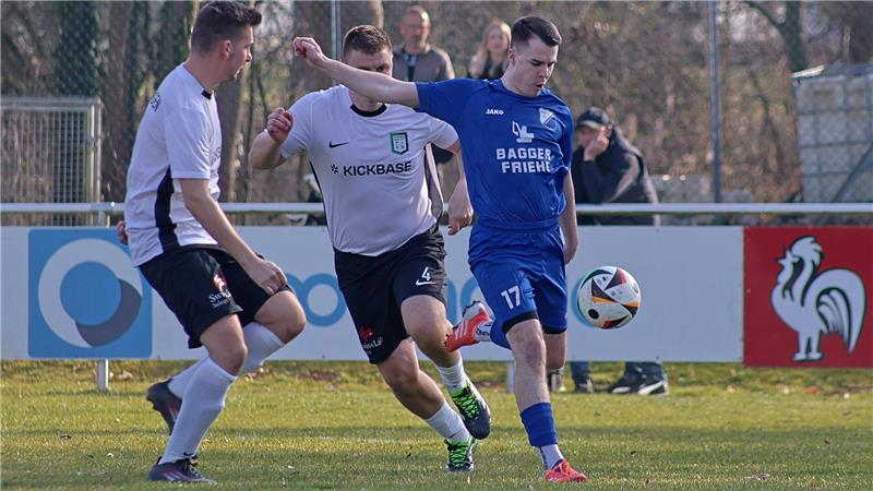 Drei Fußballspieler in Aktion auf dem Spielfeld, zwei in weißen Trikots und einer in blauem Trikot, mit Ball am Fuß