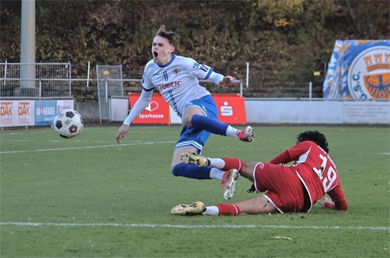 Fußballspieler in rotem Trikot rutscht auf dem Boden und bringt Spieler in weißem Trikot zu Fall