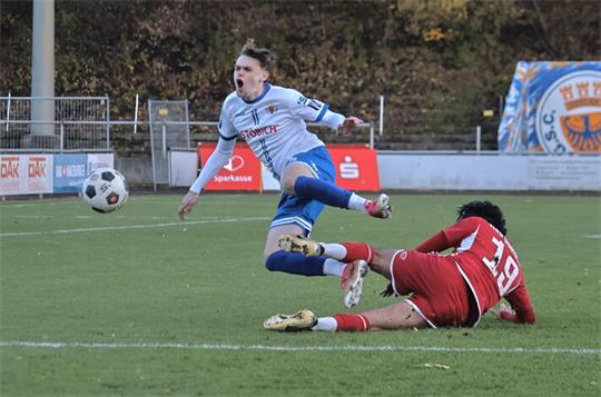 Fußballspieler in rotem Trikot rutscht auf dem Boden und bringt Spieler in weißem Trikot zu Fall