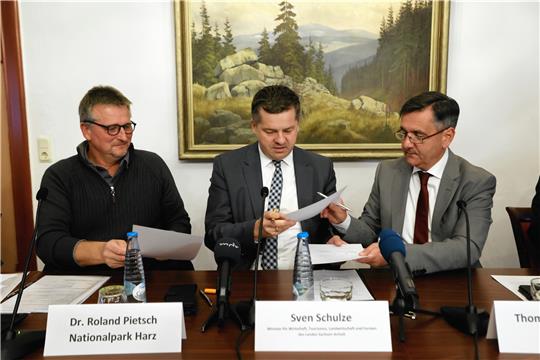 Sachsen-Anhalts Forstminister Sven Schulze (CDU, Mitte) tauscht während der Vorstellung von Maßnahmen zur Waldbrandprävention einen Vertrag mit dem Leiter des Nationalparks, Roland Pietsch (links), und dem Landrat des Landkreises Harz, Thomas Balcerowski, aus.  Foto: Bein